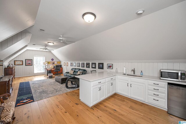 kitchen with kitchen peninsula, appliances with stainless steel finishes, vaulted ceiling, light hardwood / wood-style flooring, and white cabinets