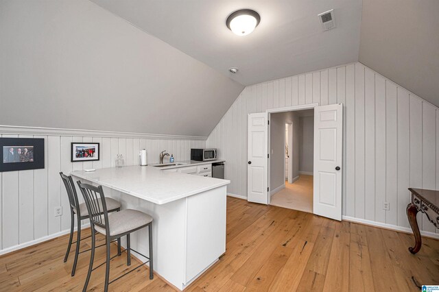 kitchen featuring kitchen peninsula, a kitchen breakfast bar, light wood-type flooring, vaulted ceiling, and sink