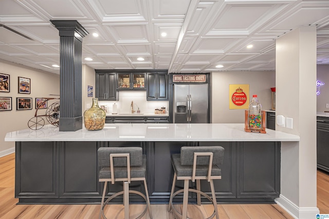 kitchen with kitchen peninsula, stainless steel fridge, light wood-type flooring, and a kitchen breakfast bar