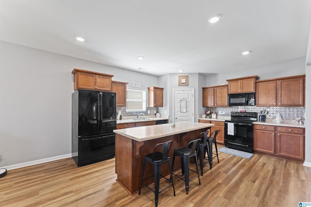 kitchen with a breakfast bar, light wood-type flooring, a kitchen island, and black appliances