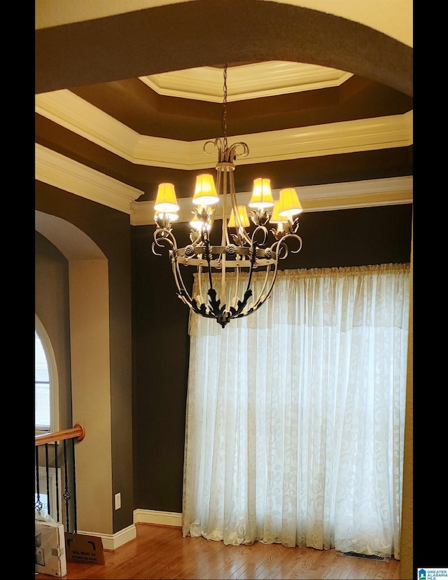 interior space with wood-type flooring, ornamental molding, a tray ceiling, and an inviting chandelier