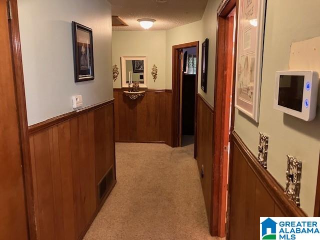 corridor with wood walls, light colored carpet, and a textured ceiling