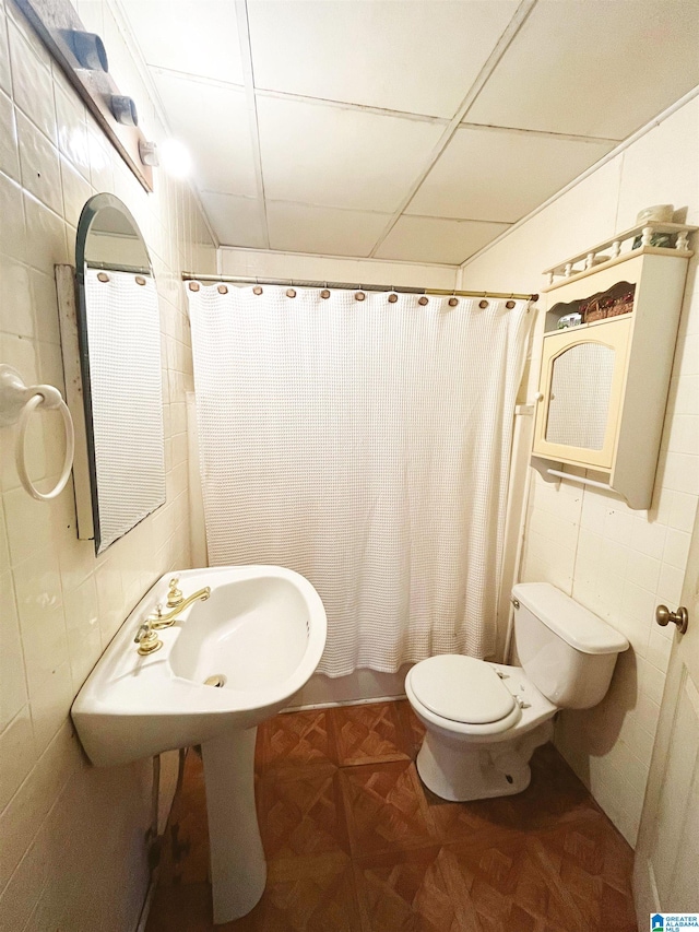 bathroom with parquet flooring, a drop ceiling, shower / bath combo with shower curtain, tile walls, and toilet