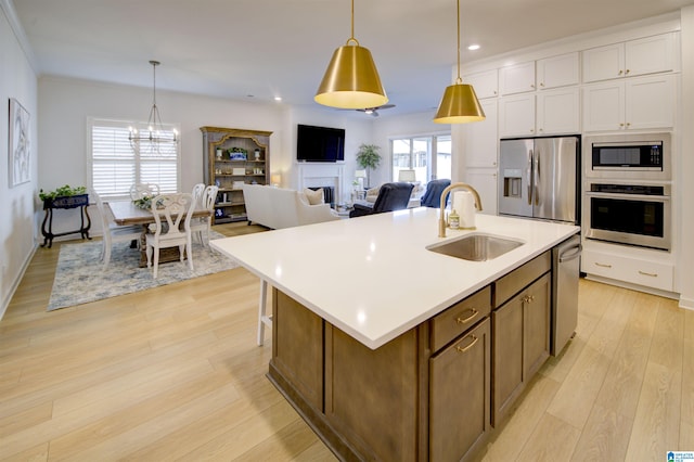 kitchen featuring appliances with stainless steel finishes, a kitchen island with sink, sink, light hardwood / wood-style flooring, and hanging light fixtures