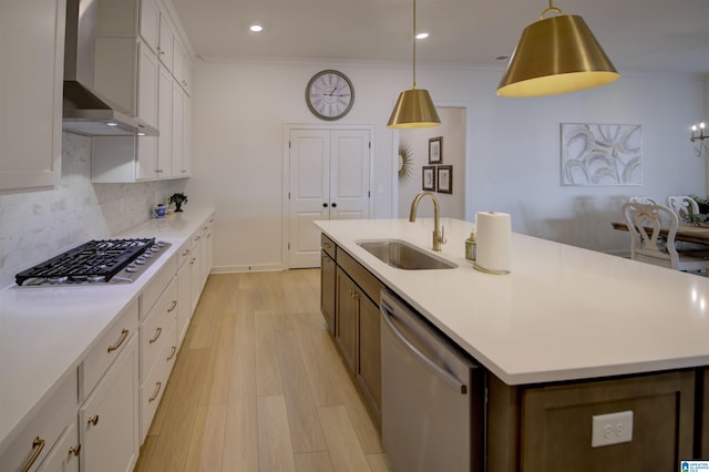 kitchen with a center island with sink, sink, wall chimney exhaust hood, appliances with stainless steel finishes, and white cabinetry