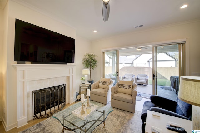 living room featuring ceiling fan, a fireplace, crown molding, and light wood-type flooring