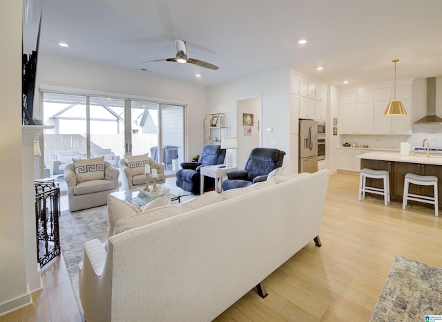 living room with light hardwood / wood-style flooring, ceiling fan, crown molding, and sink