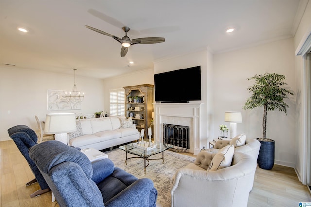 living room featuring a tile fireplace, ceiling fan with notable chandelier, light hardwood / wood-style floors, and crown molding