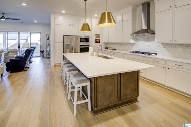 kitchen featuring appliances with stainless steel finishes, a center island with sink, wall chimney exhaust hood, and sink