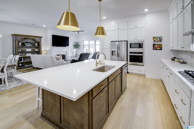 kitchen featuring sink, stainless steel appliances, light hardwood / wood-style floors, decorative light fixtures, and a kitchen island with sink