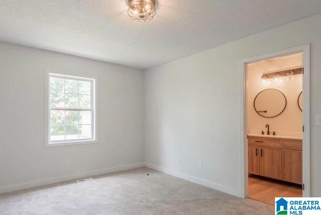 unfurnished bedroom featuring ensuite bath, sink, light colored carpet, and a textured ceiling