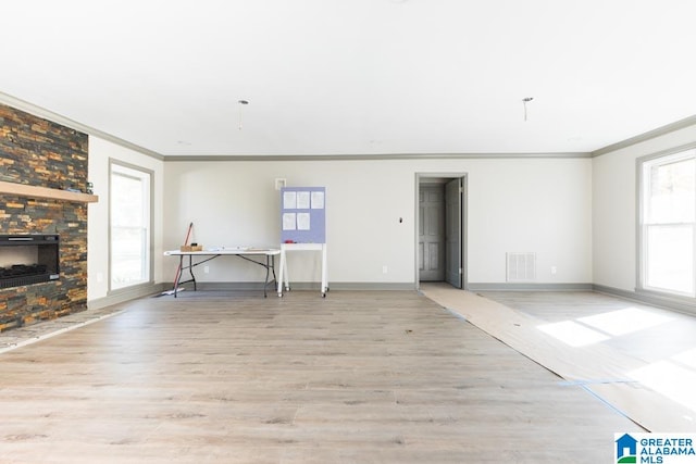 unfurnished living room featuring a stone fireplace, crown molding, and light wood-type flooring