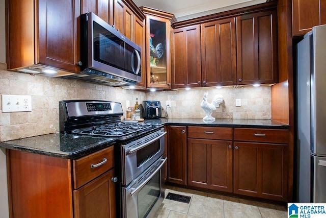 kitchen featuring light tile patterned floors, backsplash, stainless steel appliances, and dark stone counters