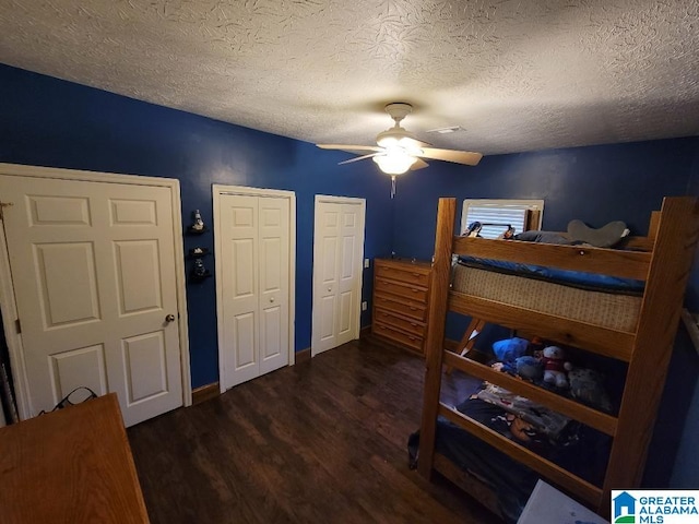 bedroom featuring ceiling fan, dark hardwood / wood-style flooring, a textured ceiling, and multiple closets