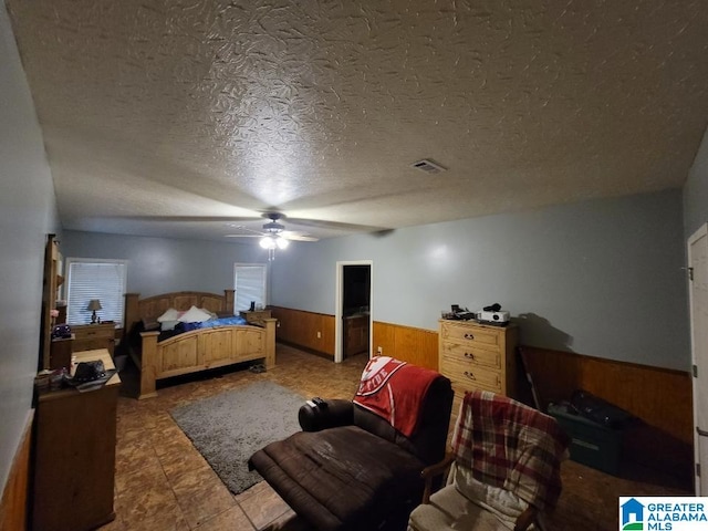 bedroom with ceiling fan, wood walls, and a textured ceiling