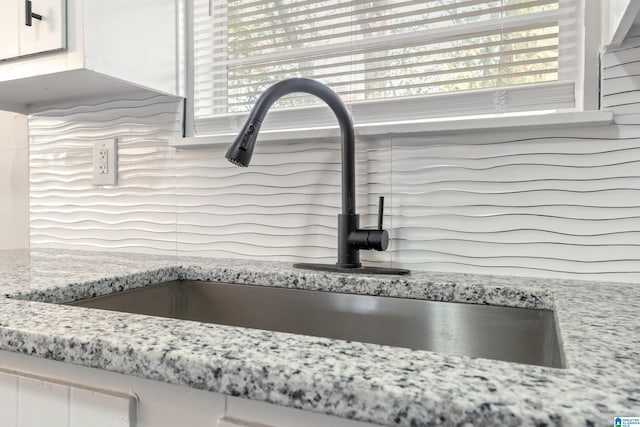 interior details featuring light stone countertops, sink, and white cabinets