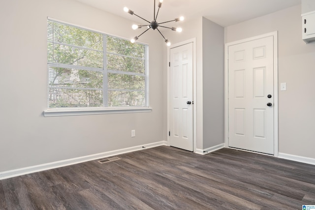 spare room with a healthy amount of sunlight, dark hardwood / wood-style flooring, and an inviting chandelier