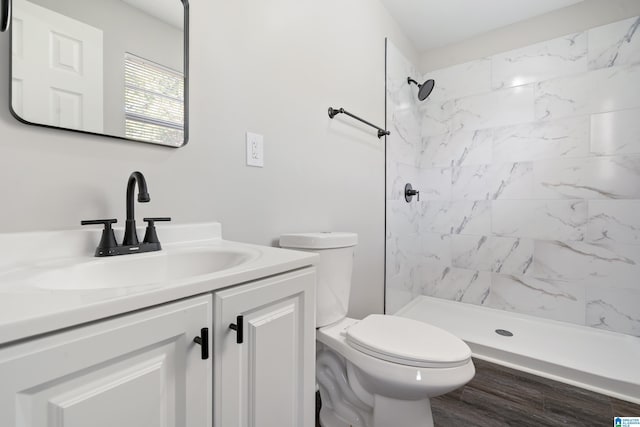 bathroom with hardwood / wood-style floors, vanity, toilet, and a tile shower