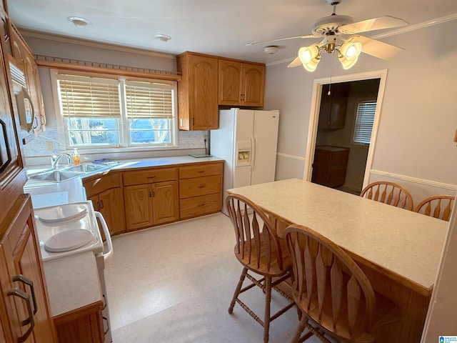 kitchen with ceiling fan, white fridge with ice dispenser, crown molding, and sink