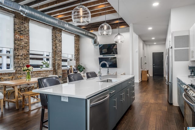 kitchen featuring sink, an island with sink, decorative light fixtures, stainless steel appliances, and brick wall