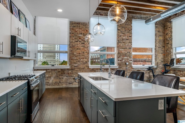 kitchen with a kitchen bar, appliances with stainless steel finishes, brick wall, sink, and a center island with sink