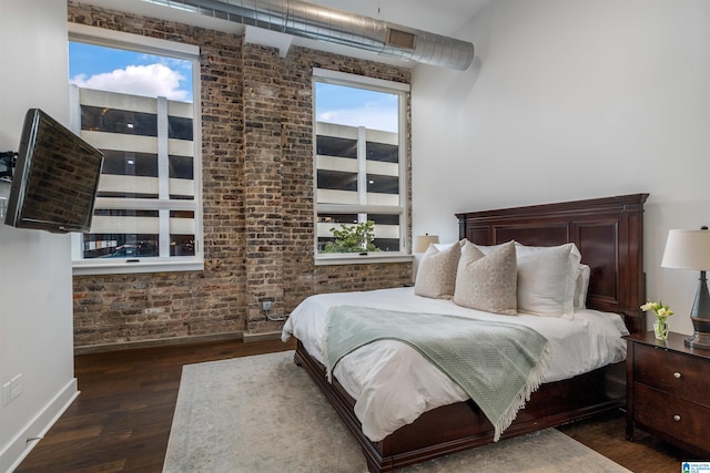 bedroom with dark wood-type flooring and brick wall