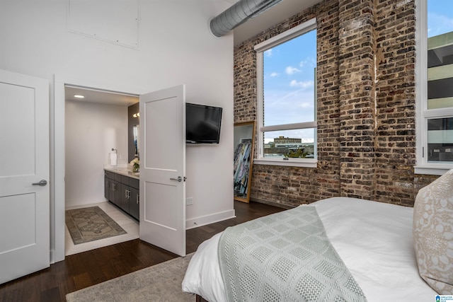 bedroom with dark hardwood / wood-style floors, brick wall, and connected bathroom