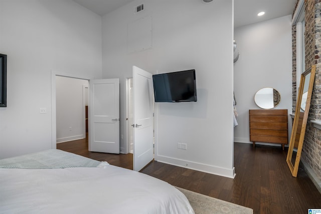 bedroom with a towering ceiling, dark wood-type flooring, and brick wall