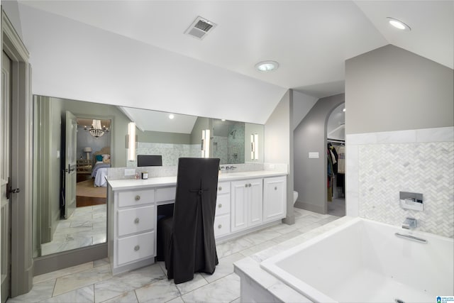 bathroom with a notable chandelier, vanity, tiled tub, and vaulted ceiling