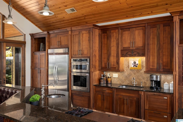 kitchen with dark stone counters, sink, pendant lighting, and appliances with stainless steel finishes