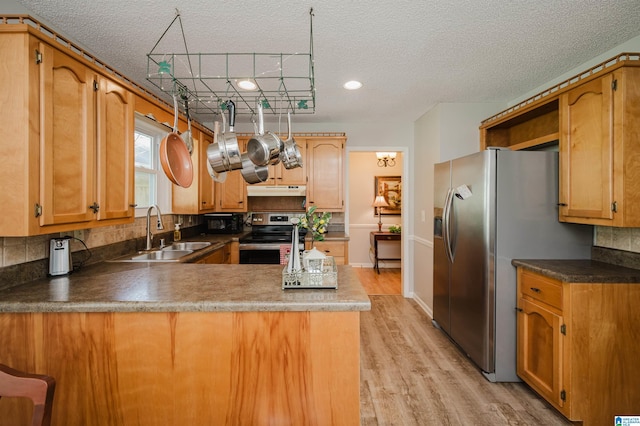 kitchen with kitchen peninsula, appliances with stainless steel finishes, a textured ceiling, sink, and light hardwood / wood-style floors