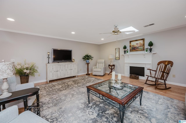 living room with a skylight, crown molding, ceiling fan, and wood-type flooring