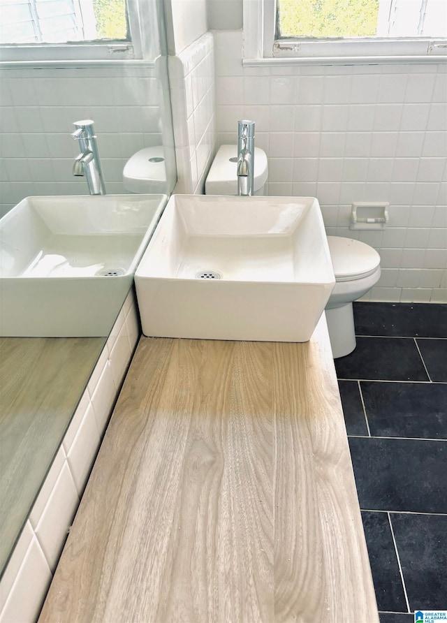 bathroom with tile patterned flooring, sink, toilet, and tile walls