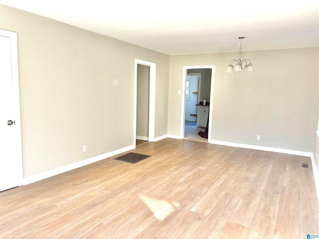 empty room with light wood-type flooring and a chandelier