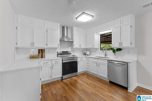 kitchen with white cabinets, appliances with stainless steel finishes, hardwood / wood-style flooring, and wall chimney range hood