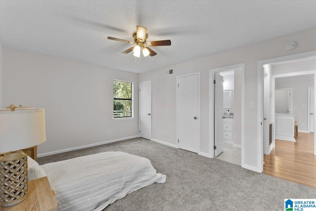 bedroom with a textured ceiling, ceiling fan, light carpet, and connected bathroom