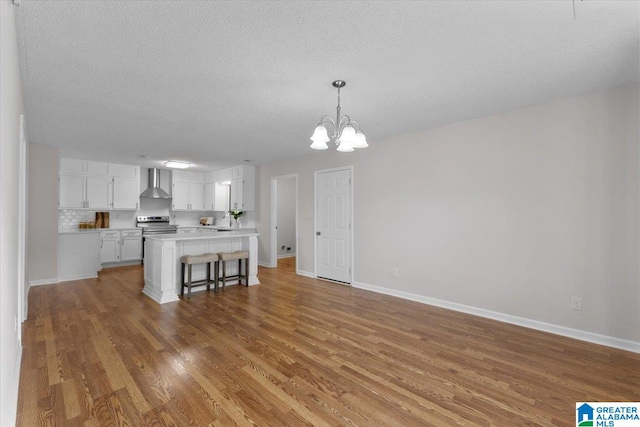 kitchen with white cabinetry, wall chimney exhaust hood, hanging light fixtures, a kitchen breakfast bar, and wood-type flooring