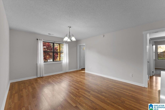 spare room with a textured ceiling, plenty of natural light, dark wood-type flooring, and a chandelier