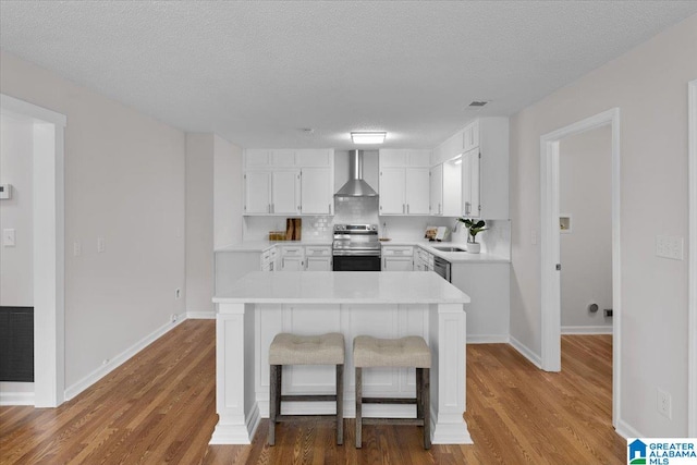 kitchen with wall chimney exhaust hood, stainless steel electric range, white cabinetry, and wood-type flooring