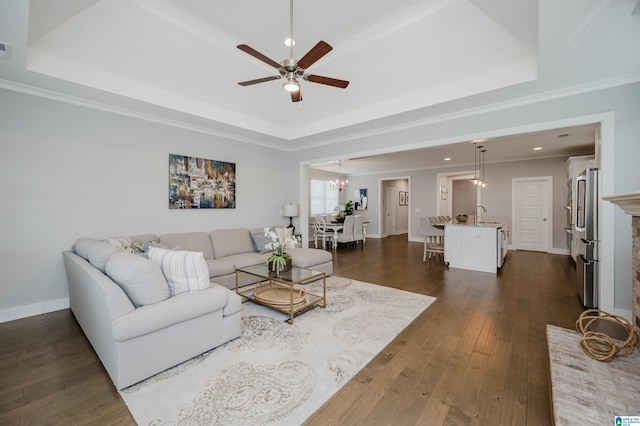 living room featuring dark hardwood / wood-style floors, crown molding, ceiling fan, and a tray ceiling