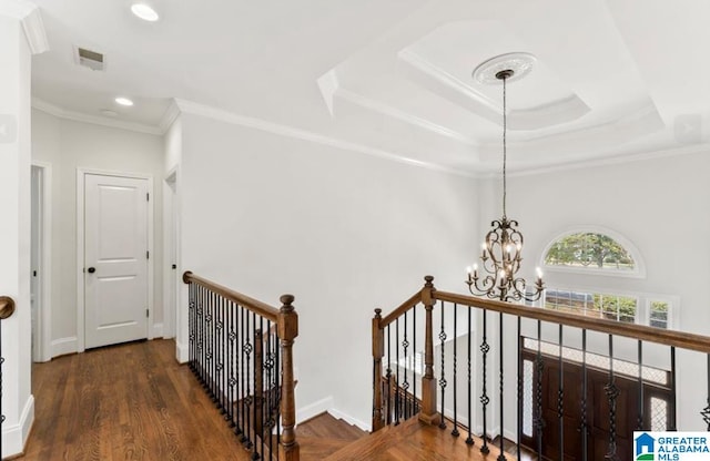 stairs with a raised ceiling, hardwood / wood-style floors, ornamental molding, and a notable chandelier