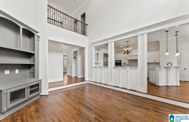 unfurnished living room with built in features, a towering ceiling, dark wood-type flooring, and a notable chandelier