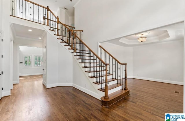 staircase featuring ornamental molding, a tray ceiling, hardwood / wood-style flooring, a notable chandelier, and a high ceiling