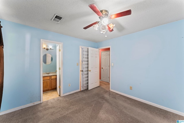 unfurnished bedroom featuring a textured ceiling, ensuite bathroom, ceiling fan, and light colored carpet