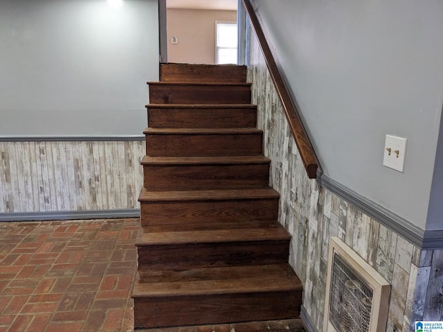 staircase featuring a high ceiling, wooden walls, and heating unit