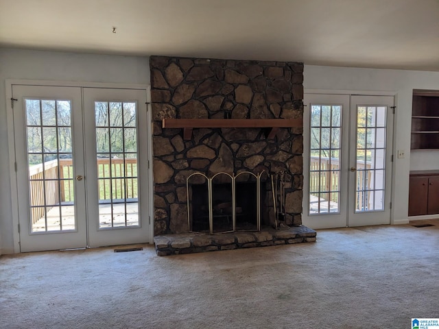 unfurnished living room with carpet flooring, a stone fireplace, and french doors