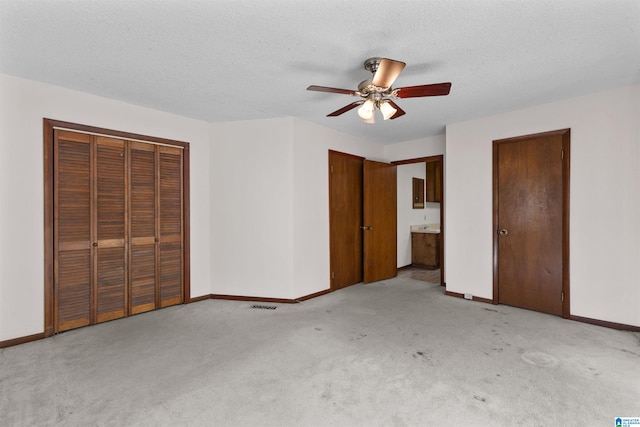 unfurnished bedroom with ceiling fan, ensuite bathroom, light colored carpet, and a textured ceiling