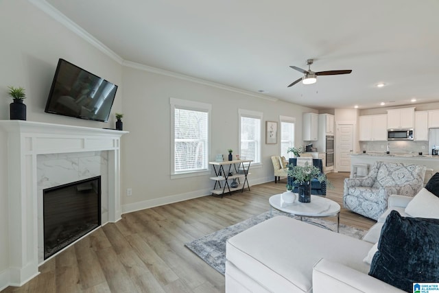 living room featuring light hardwood / wood-style floors, ceiling fan, ornamental molding, and a premium fireplace