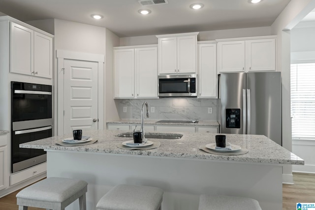 kitchen with light hardwood / wood-style floors, white cabinets, an island with sink, and appliances with stainless steel finishes