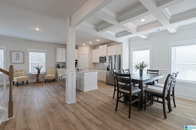 dining space with beam ceiling, sink, a healthy amount of sunlight, and light wood-type flooring